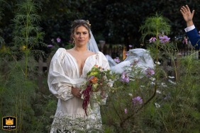 Bride's Radiance and Groom's Fun Gesture Captured in Beautiful Decatur Wedding Photo A joyful bride beams as her groom playfully flings her veil into the air, surrounded by vibrant flowers at their family home in Decatur.